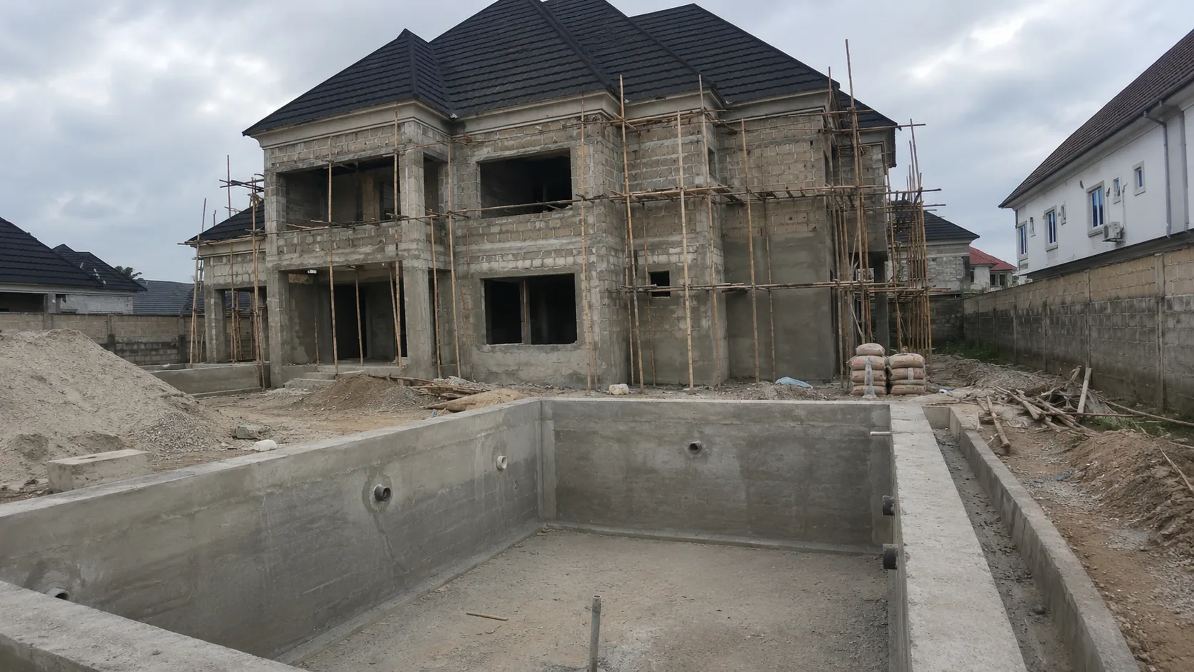 Swimming pool shell under construction beside a two-storey residence